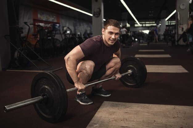 Szczęśliwy przystojny cross fit lekkoatleta uśmiecha się do kamery podczas ćwiczeń ze sztangą