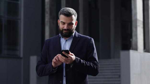 Szczęśliwy przystojny mężczyzna za pomocą aplikacji na telefony komórkowe, wiadomości tekstowe, przeglądanie internetu, patrząc na smartfona.