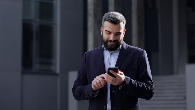 Szczęśliwy przystojny mężczyzna za pomocą aplikacji na telefony komórkowe, wiadomości tekstowe, przeglądanie internetu, patrząc na smartfona.