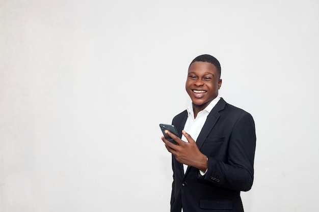 Zdjęcie szczęśliwy, przystojny, zdumiony afrykański biznesmen w czarnym garniturze, korzystający z czatu na smartfonie
