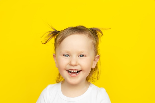 Szczęśliwy radosny śmiech małej dziewczynki w białej koszuli na żółtym tle