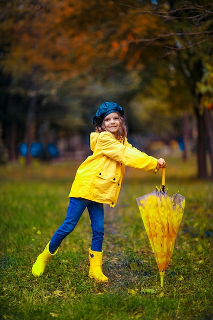 Szczęśliwy śmieszne dziecko dziewczynka z parasolem multicolor w kalosze w parku jesienią.