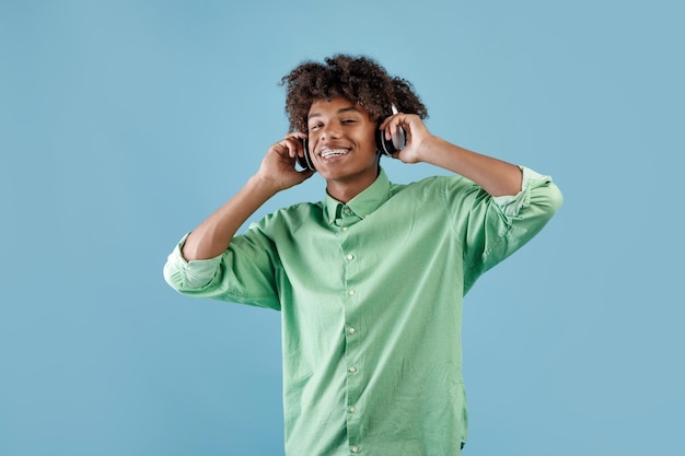 Szczęśliwy spokojny Afroamerykanin słuchający muzyki w bezprzewodowym zestawie słuchawkowym, zamykający oczy i relaksujący