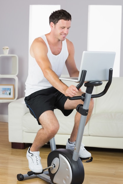 Szczęśliwy sportowy mężczyzna ćwiczy na rowerze i używa laptop