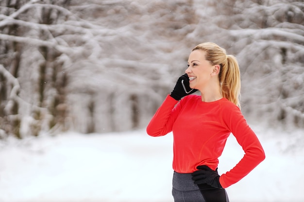 Szczęśliwy sportsmenka stoi w przyrodzie w mroźny zimowy dzień i rozmawia przez telefon w przerwie. Telekomunikacja, zdrowy tryb życia, fitness zimowy