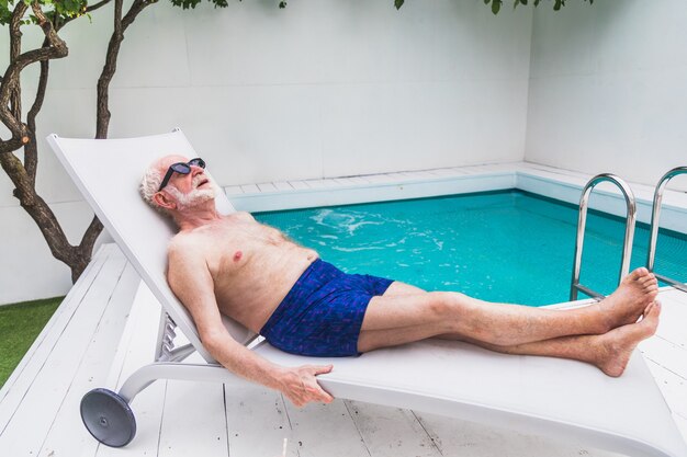 Szczęśliwy starszy mężczyzna imprezujący w basenie - Aktywny starszy mężczyzna opalający się i relaksujący w prywatnym basenie latem
