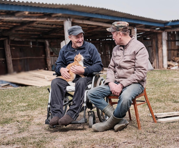 Zdjęcie szczęśliwy starszy mężczyzna na wózku inwalidzkim na podwórku uśmiecha się trzymając uroczego kota rozmawiającego ze swoim przyjacielem