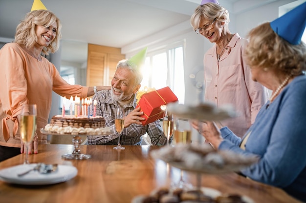 Szczęśliwy starszy mężczyzna odbiera prezent od swoich przyjaciół na przyjęciu urodzinowym w domu