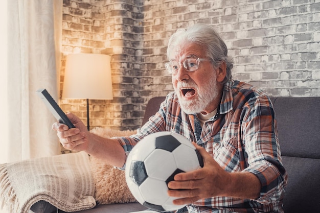 Szczęśliwy stary senior lub fani piłki nożnej oglądający piłkę nożną w telewizji i świętujący zwycięstwo w domu Euforyczne pojęcie sportu i rozrywki