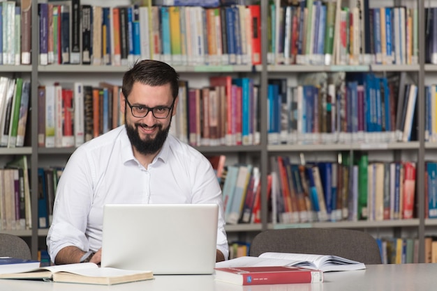 Szczęśliwy student z laptopem w bibliotece