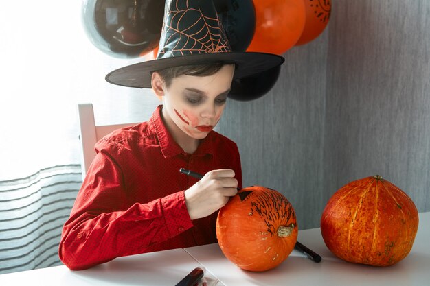 Szczęśliwy teen chłopiec w kostiumie przygotowuje się do obchodów Halloween rysowanie dyni