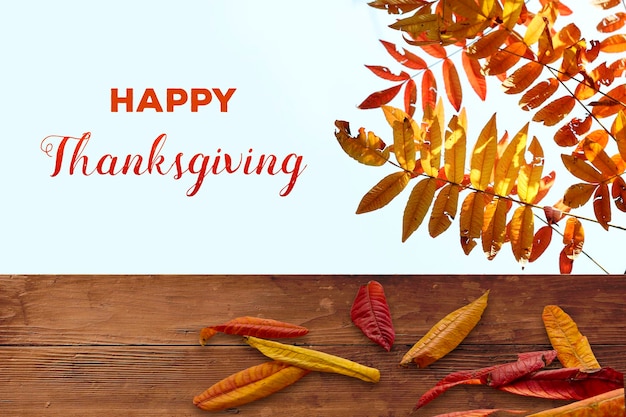 Szczęśliwy tekst Dziękczynienia na niebie z kolorowymi jesiennymi liśćmi nad drewnianym stołem
