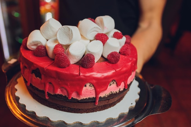 Szczęśliwy tort z okazji Dnia Kanady z flagami marshmallow i dekoracjami z cukierków na czerwonym stojaku na ciasto na białym stole na czerwonym tle