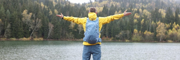 Szczęśliwy turysta stoi z otwartymi ramionami na skale nad jeziorem i patrzy na wzgórza podróżujące na świeżym powietrzu