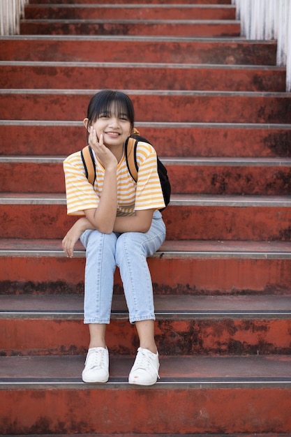 Szczęśliwy uczeń nosi żółtą koszulę i dżinsy z plecakiem, siedząc na schodach w szkole.
