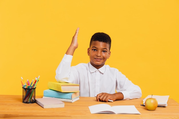 Szczęśliwy uczeń rasy mieszanej siedzi przy biurku i wyciąga rękę podczas lekcji Powrót do koncepcji szkoły