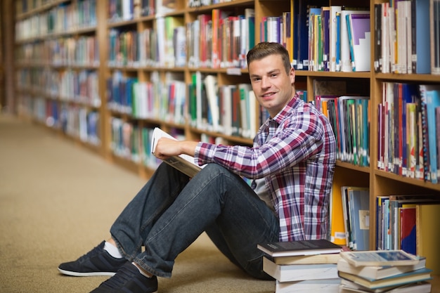 Szczęśliwy uczeń siedzi na podłodze biblioteki czytanie