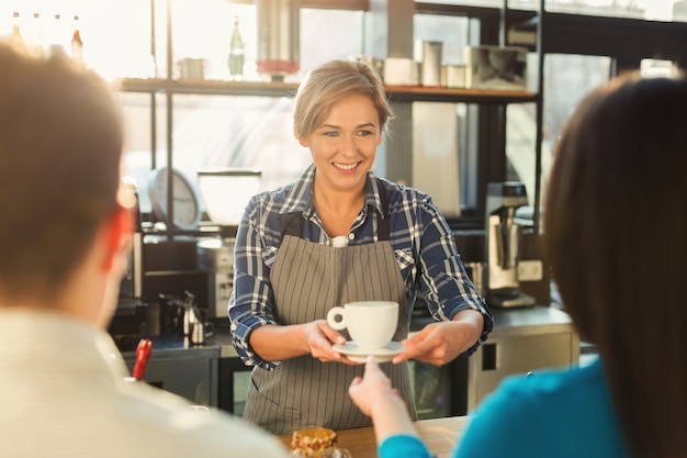 Szczęśliwy uśmiechający się barista robi kawę i rozmawia z gośćmi przy barze. Doświadczona barmanka zapraszająca para. Mały biznes, koncepcja ludzi i usług, kopia przestrzeń