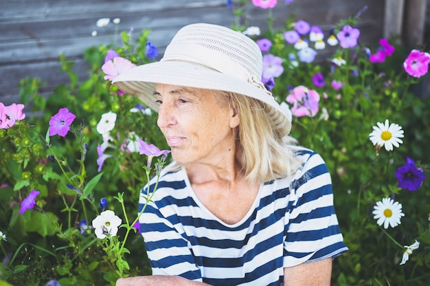 Szczęśliwy uśmiechający się starszy kobieta pozuje w letnim ogrodzie z kwiatami