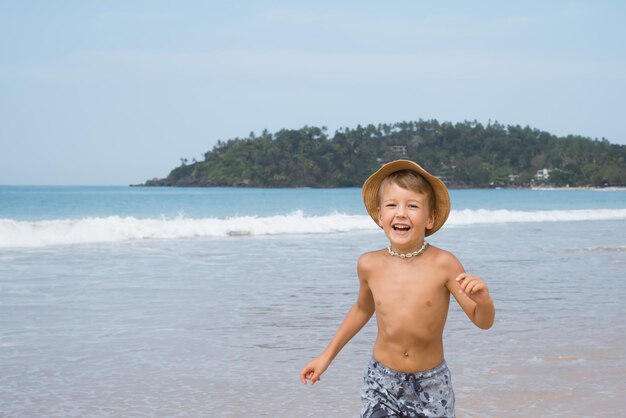 Zdjęcie szczęśliwy uśmiechnięty chłopiec przedszkolny biegający po piasku na plaży w gorący słoneczny dzień