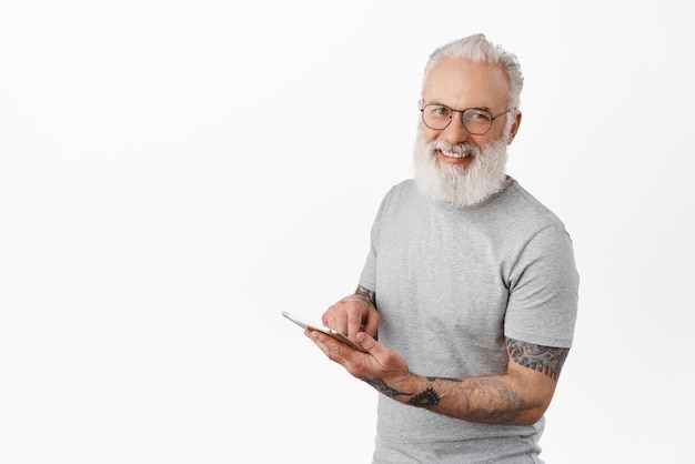 Szczęśliwy uśmiechnięty dziadek w okularach za pomocą cyfrowego tabletu robiący zakupy online stojący w szarej koszulce na białym tle