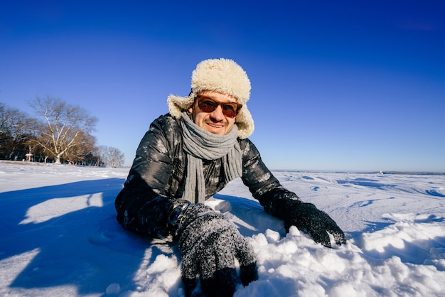 Szczęśliwy uśmiechnięty mężczyzna w okularach przeciwsłonecznych, stwarzających w śniegu na zewnątrz