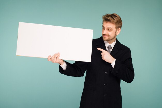 Szczęśliwy uśmiechnięty młody człowiek biznesu wskazuje palcem pustą tablicę, na niebiesko