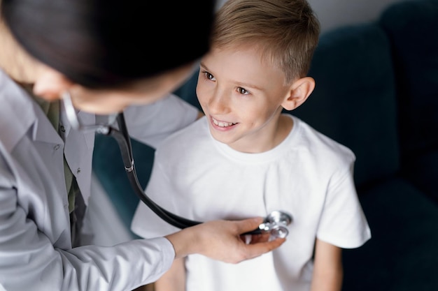 Zdjęcie szczęśliwy uśmiechnięty pacjent w zwykłej inspekcji medycznej lekarz i chłopiec w domu koncepcje opieki zdrowotnej medycyny