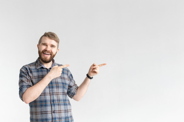 Zdjęcie szczęśliwy zabawny hipster młody człowiek z wąsem, pozowanie na białym tle i wskazując na prawo