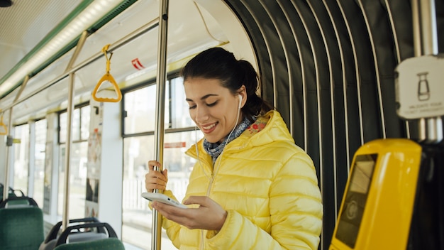 Szczęśliwy żeński pasażer słucha muzyka na smartphone transporcie publicznie.