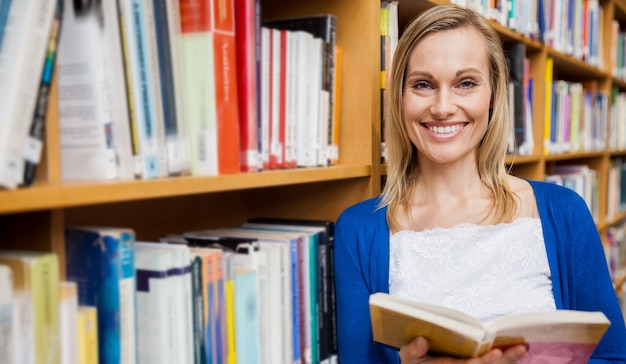 Szczęśliwy żeński uczeń czyta książkę w bibliotece przy uniwersytetem