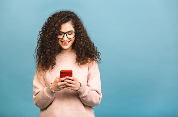 Szczęśliwy Zwycięzca! Portret Zaskoczony Zdumiony Uśmiechnięty Dorywczo Kręcone Studentki Kobieta Trzyma Smartfon Na Białym Tle Na Niebieskim Tle.