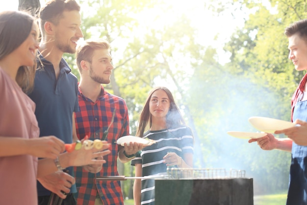 Szczęśliwych przyjaciół grillujących mięso i cieszących się grillem na świeżym powietrzu.