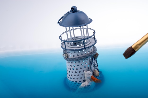 Szczotka do malowania i mały model latarni umieszczony w niebieskiej wodzie