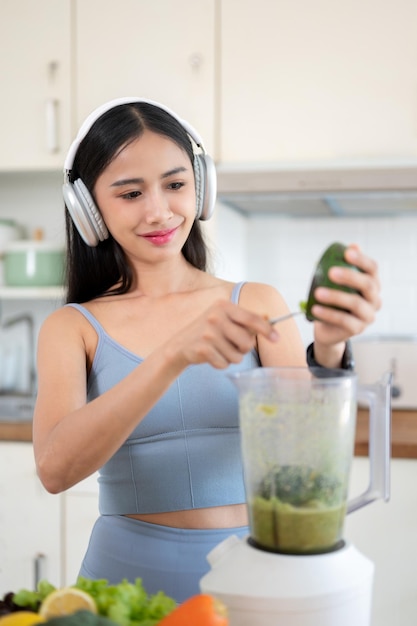 Szczupła Azjatka w stroju gimnastycznym i słuchawkach robi zdrowy zielony koktajl