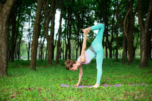 Szczupła Brunetka Uprawia Sport I Wykonuje Piękne I Wyrafinowane Pozy Jogi W Letnim Parku