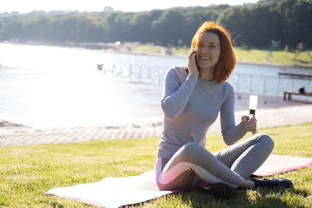 Szczupła kobieta imbir w ubrania sportowe przy użyciu telefonu komórkowego w parku. Zdrowie, wellness, styl życia fitness.