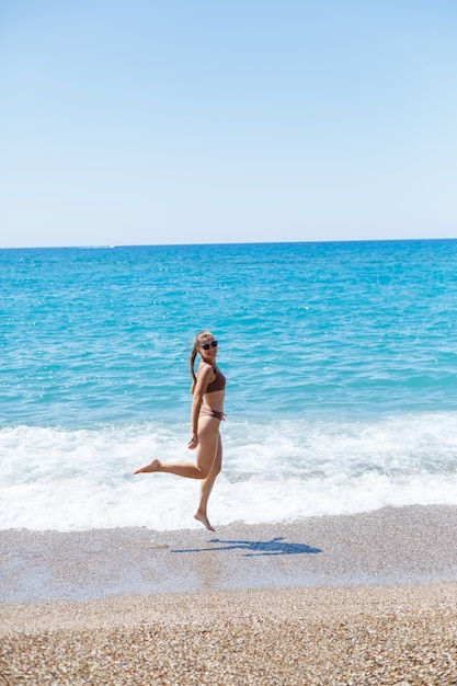 Szczupła piękna młoda kobieta w stroju kąpielowym spaceruje po plaży nad morzem. Koncepcja wakacji letnich. Selektywne skupienie