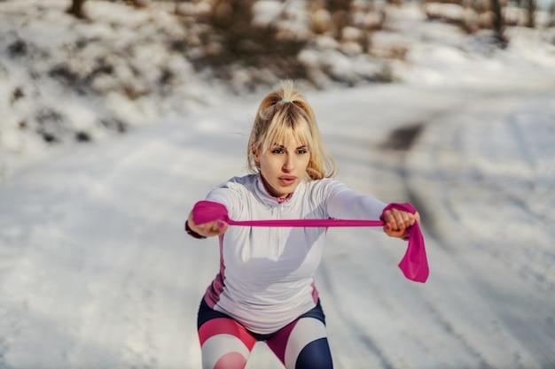 Szczupła Sportsmenka Robi ćwiczenia Z Gumy Siłowej Stojąc Na łonie Natury W śnieżny Zimowy Dzień.
