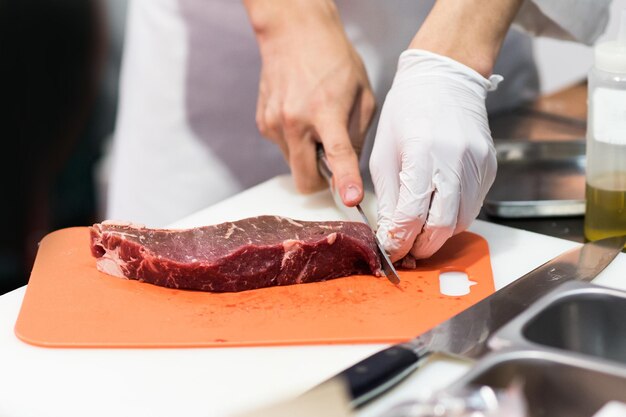 Szef kuchni cięcie świeżego surowego mięsa nożem w kuchni Szef kuchenny cięcie wołowiny na desce