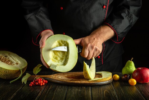 Szef kuchni cięje melon nożem w kuchni Koncepcja diety owocowej na ciemnym tle Kuchnia azjatycka