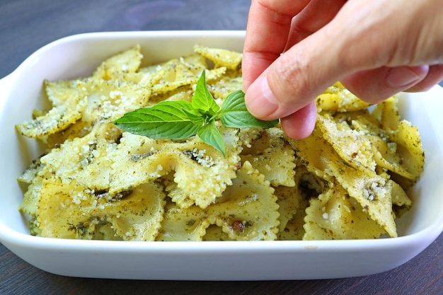 Szef kuchni dekoruje przepyszny makaron Pesto Farfalle świeżymi liśćmi bazylii