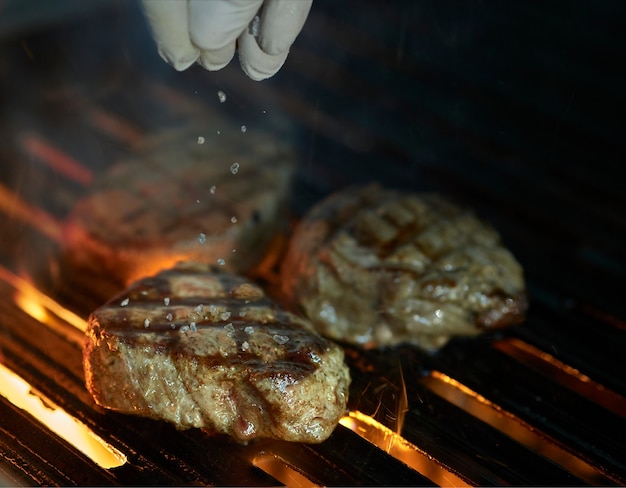 Szef kuchni dodaje sól do środka grillowanego steku z płomieniami i dymem