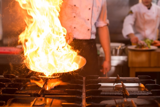Szef kuchni gotuje i robi flambe na jedzeniu w kuchni restauracji