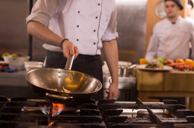 Szef kuchni gotuje i robi flambe na jedzeniu w kuchni restauracji