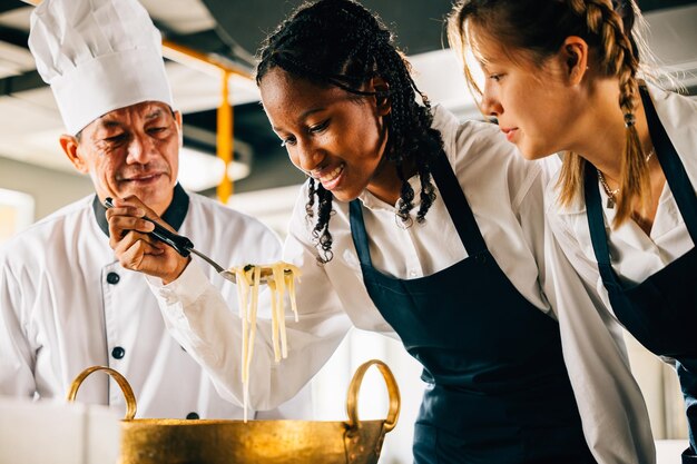 Szef kuchni instruuje dzieci do gotowania makaronów w kuchni Uczennice w mundurach tworzą zupę ramen Nauczycielka prowadzi uśmiechniętych uczniów Współczesna edukacja widziana w przygotowywaniu obiadu Koncepcja edukacji