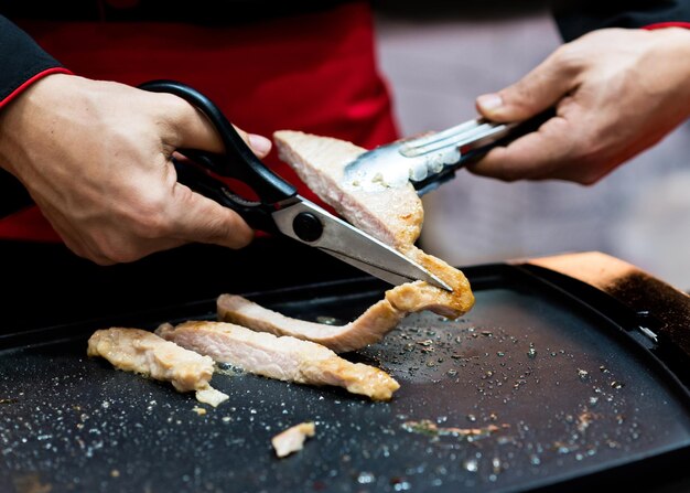 Szef kuchni jest grillowany stek wieprzowy Ręka trzyma nożyczki cięcie grillowanego steka wieprzowego