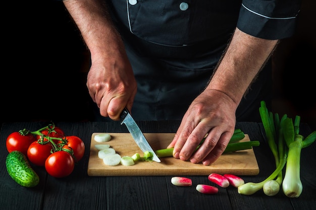 Szef kuchni jest zbliżenie ręce tnie młode zielone cebule na desce do krojenia kuchni restauracji na sałatkę. Pomysł na dietę warzywną lub przekąskę.