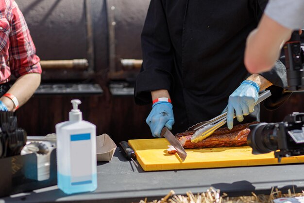 Szef kuchni kroi pyszne mięso z grilla na targu ulicznym na stole z środkiem dezynfekującym Festiwal żywności ulicznej