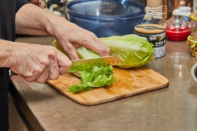 Szef kuchni kroi sałatę na drewnianej desce w domowej kuchni